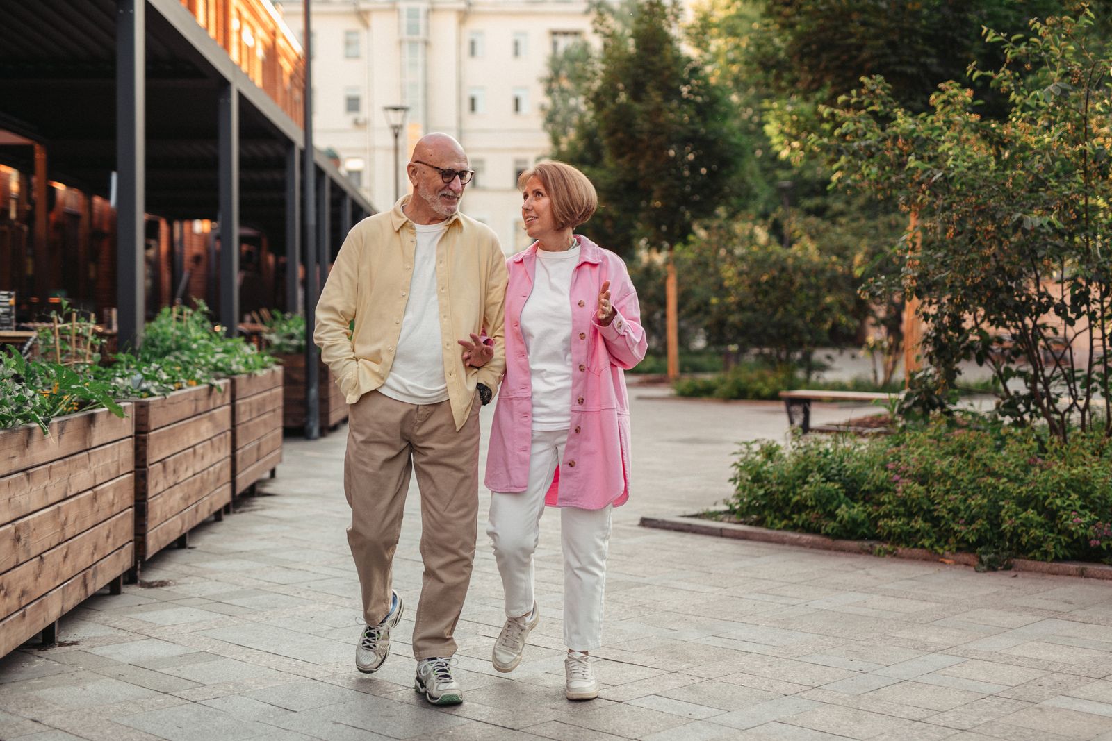 An older couple walking arm in arm in a leafy park.